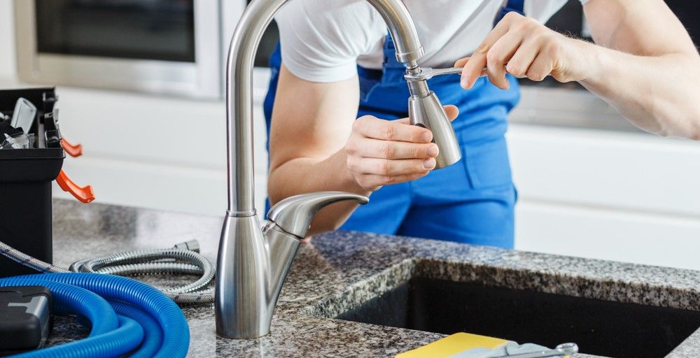 A plumber installing a new faucet on a kitchen sink